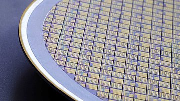 Silicon wafer covered with a pattern of intricate, colorful designs. The wafer is partially visible, with a metallic edge surrounding it.